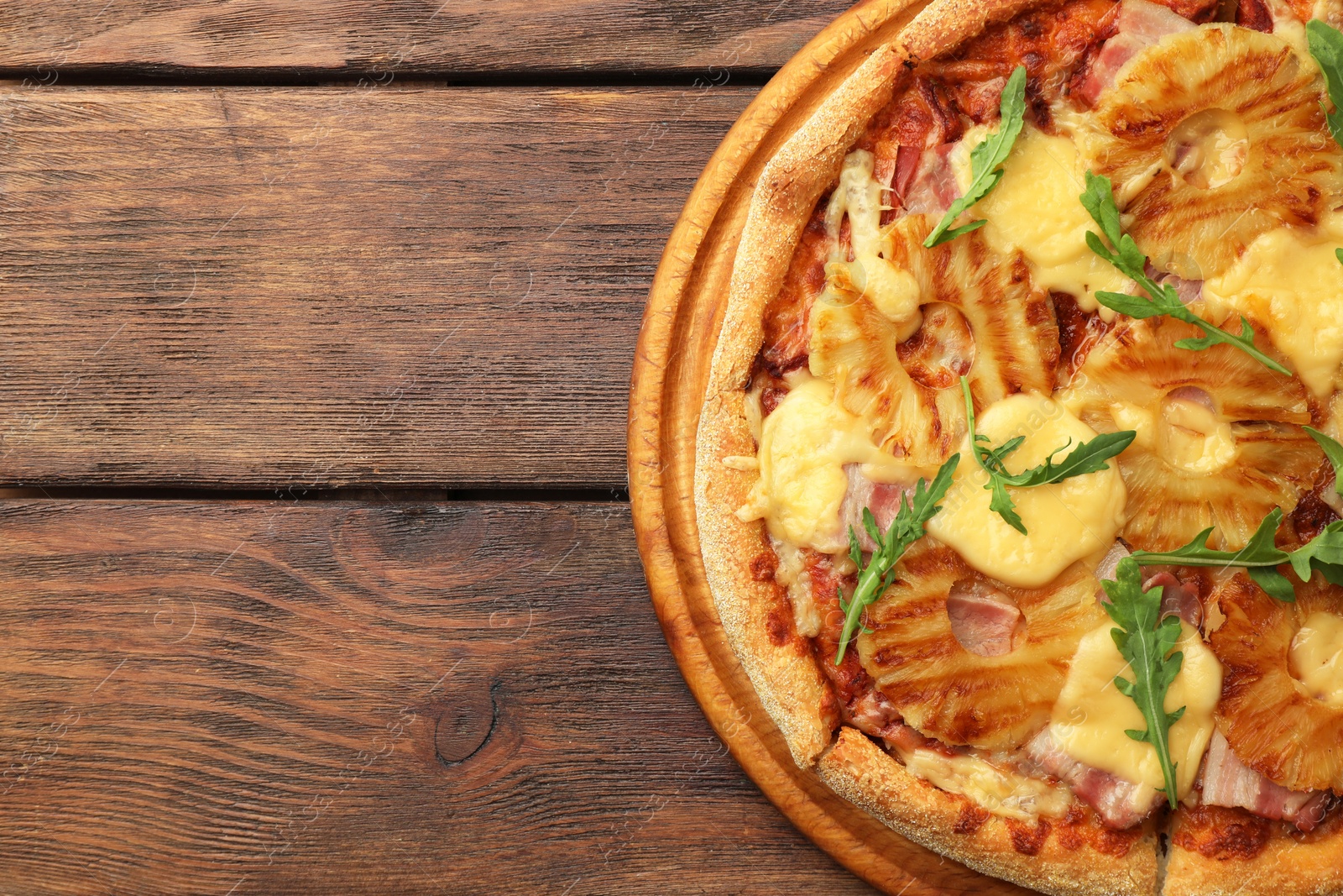 Photo of Delicious pineapple pizza with arugula on wooden table, top view. Space for text