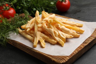 Photo of Delicious French fries with cheese sauce, tomatoes and dill on black table, closeup