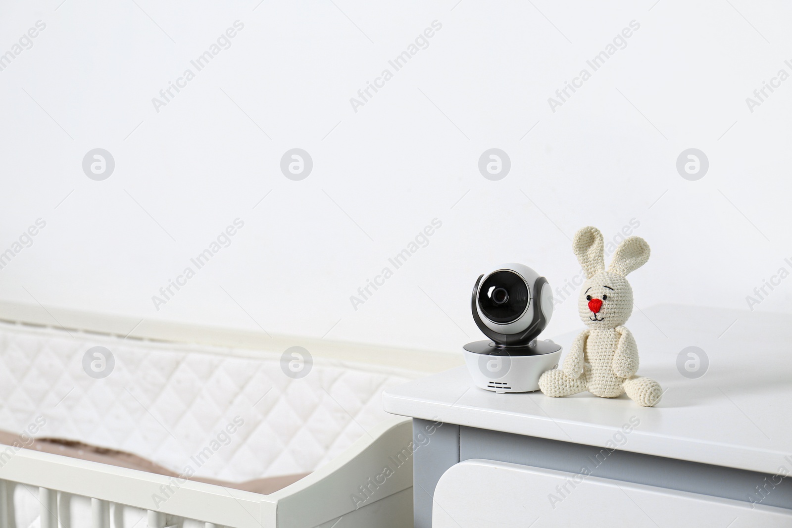 Photo of Baby camera with toy on chest of drawers near crib in room, space for text. Video nanny