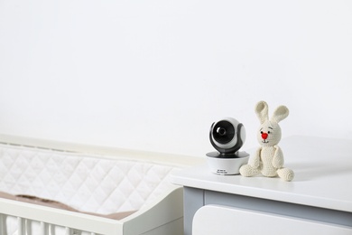 Photo of Baby camera with toy on chest of drawers near crib in room, space for text. Video nanny