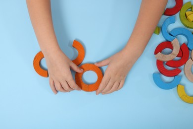 Photo of Motor skills development. Girl playing with colorful wooden arcs at light blue table, top view