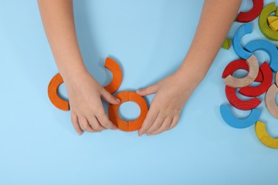 Motor skills development. Girl playing with colorful wooden arcs at light blue table, top view