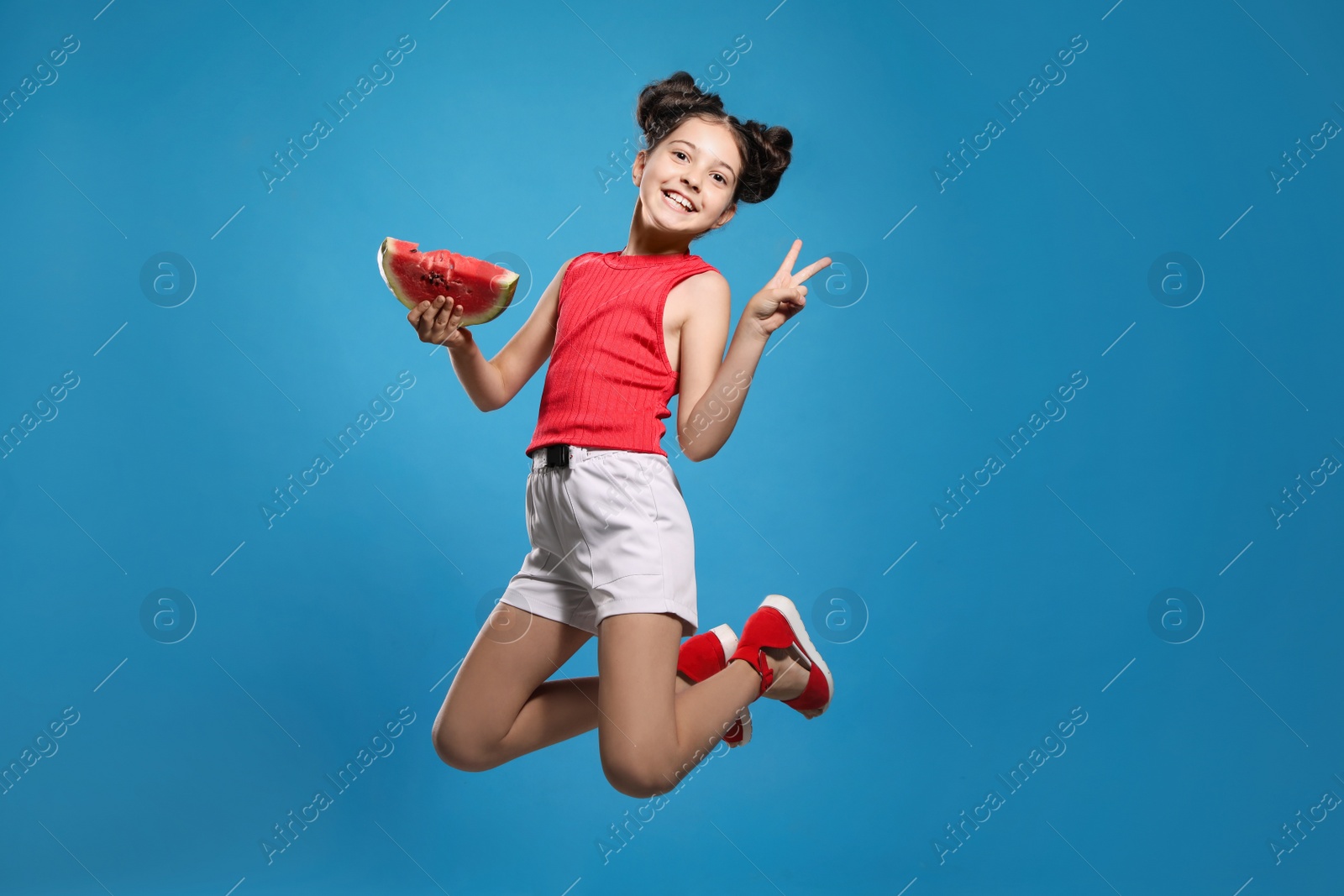 Photo of Cute little girl with watermelon jumping on blue background