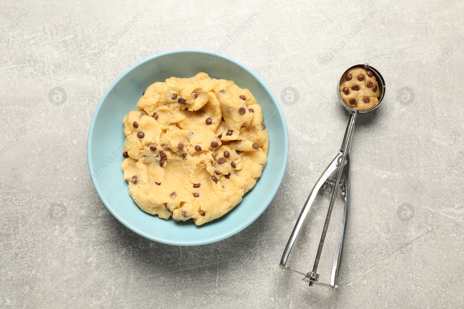 Photo of Bowl with dough for chocolate chip cookies and scoop on light grey table, flat lay