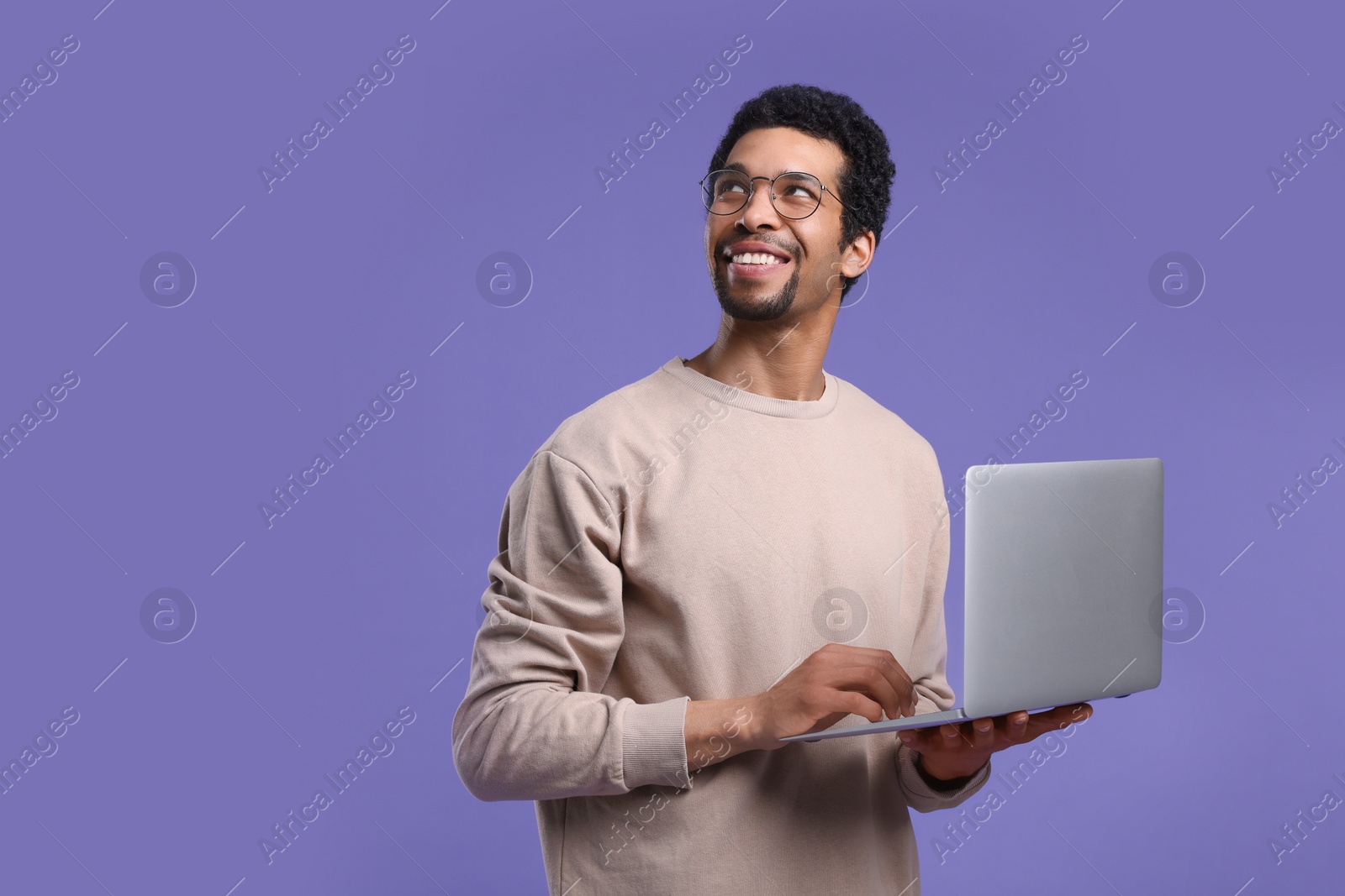 Photo of Smiling man with laptop on purple background. Space for text