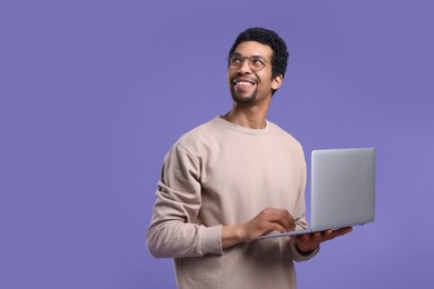 Photo of Smiling man with laptop on purple background. Space for text