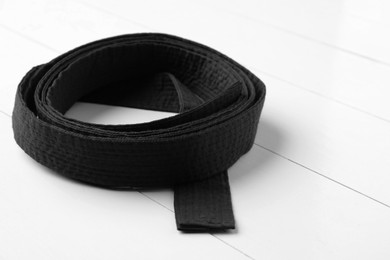 Photo of Rolled black belt on white wooden background, closeup. Oriental martial arts