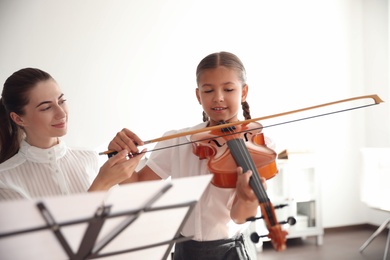 Young woman teaching little girl to play violin indoors