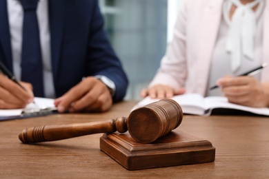 Photo of Wooden gavel and blurred lawyer with client on background