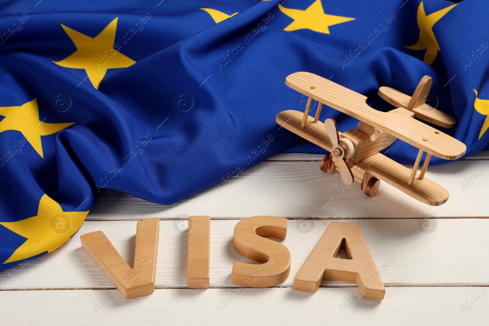 Photo of Word Visa, wooden toy plane and flag of European Union on white table