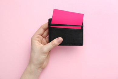 Woman holding business card holder with colorful cards on pink background, top view
