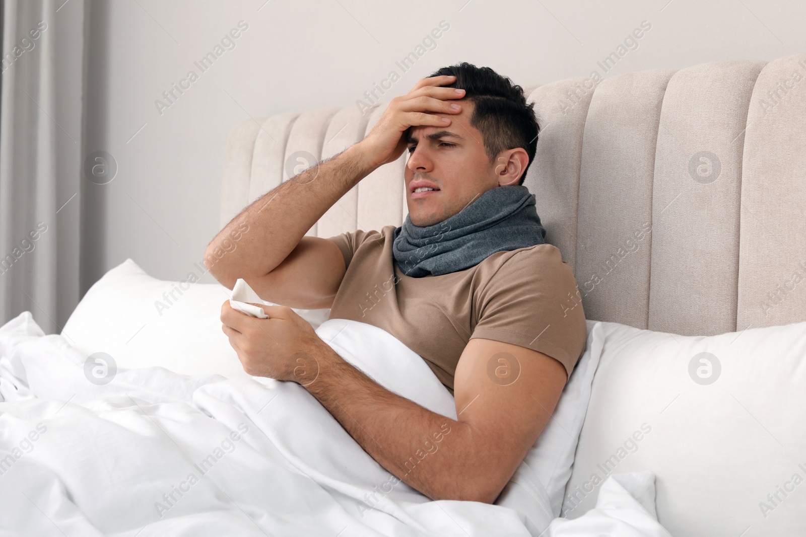 Photo of Sick man with scarf and tissue suffering from cold in bed at home