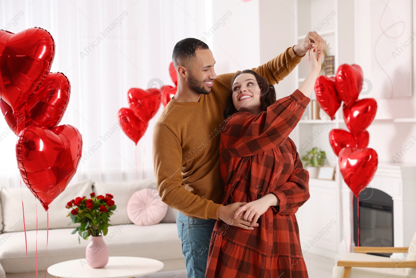 Photo of Lovely couple dancing in room decorated with heart shaped air balloons. Valentine's day celebration