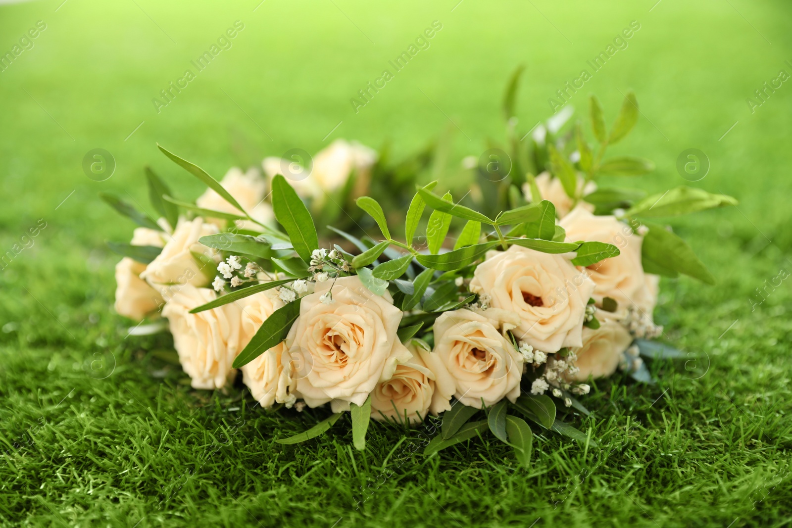 Photo of Wreath made of beautiful flowers on green grass outdoors