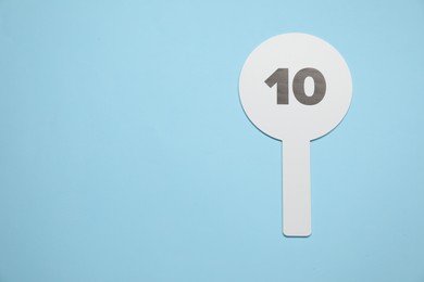 Photo of Auction paddle with number 10 on light blue background, top view. Space for text