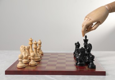 Photo of Robot playing chess against light grey background, closeup. Wooden hand representing artificial intelligence