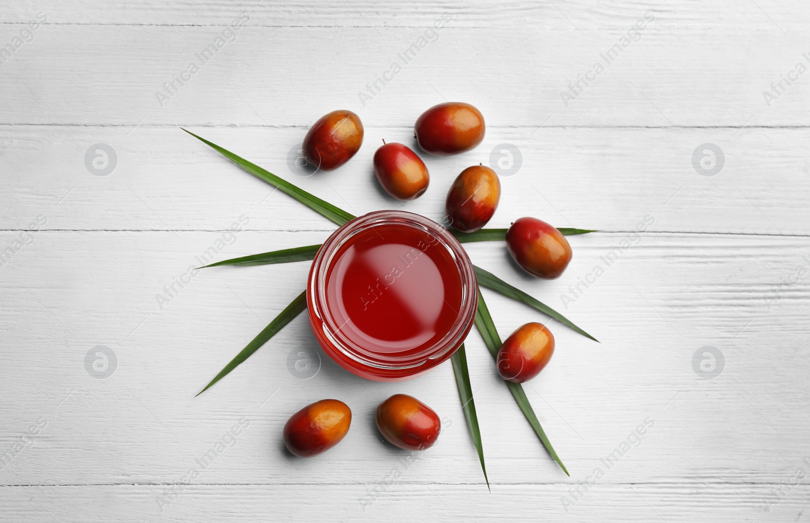 Photo of Palm oil in glass jar, tropical leaf and fruits on white wooden table, flat lay