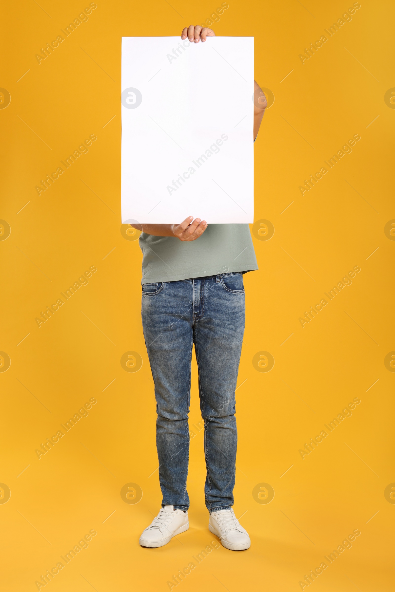 Photo of Man holding white blank poster on yellow background. Mockup for design