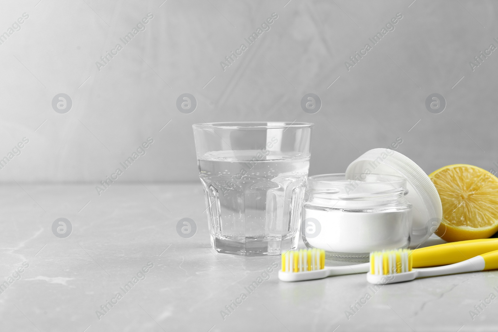 Photo of Toothbrushes, lemon and jar of baking soda on light grey table, space for text