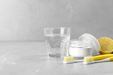 Photo of Toothbrushes, lemon and jar of baking soda on light grey table, space for text
