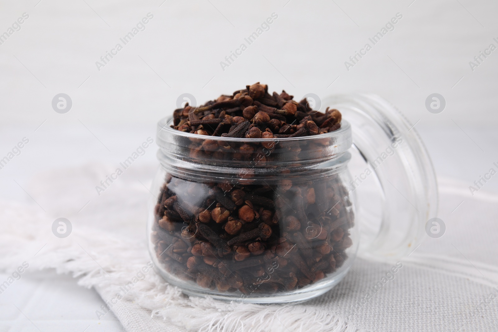 Photo of Aromatic cloves in glass jar on white table, closeup