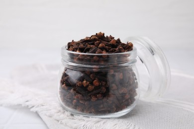 Photo of Aromatic cloves in glass jar on white table, closeup