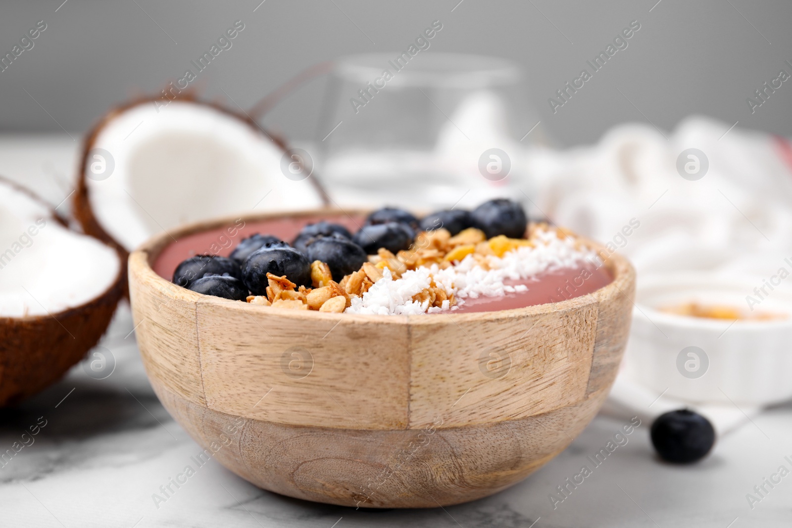 Photo of Bowl of delicious fruit smoothie with fresh blueberries, granola and coconut flakes on white marble table, closeup