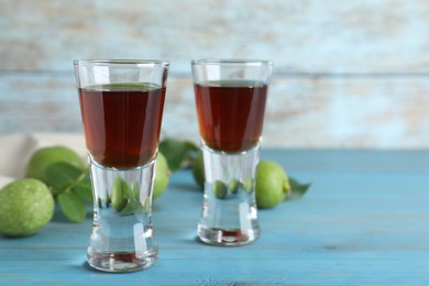 Photo of Delicious liqueur and green walnuts on light blue wooden table, space for text