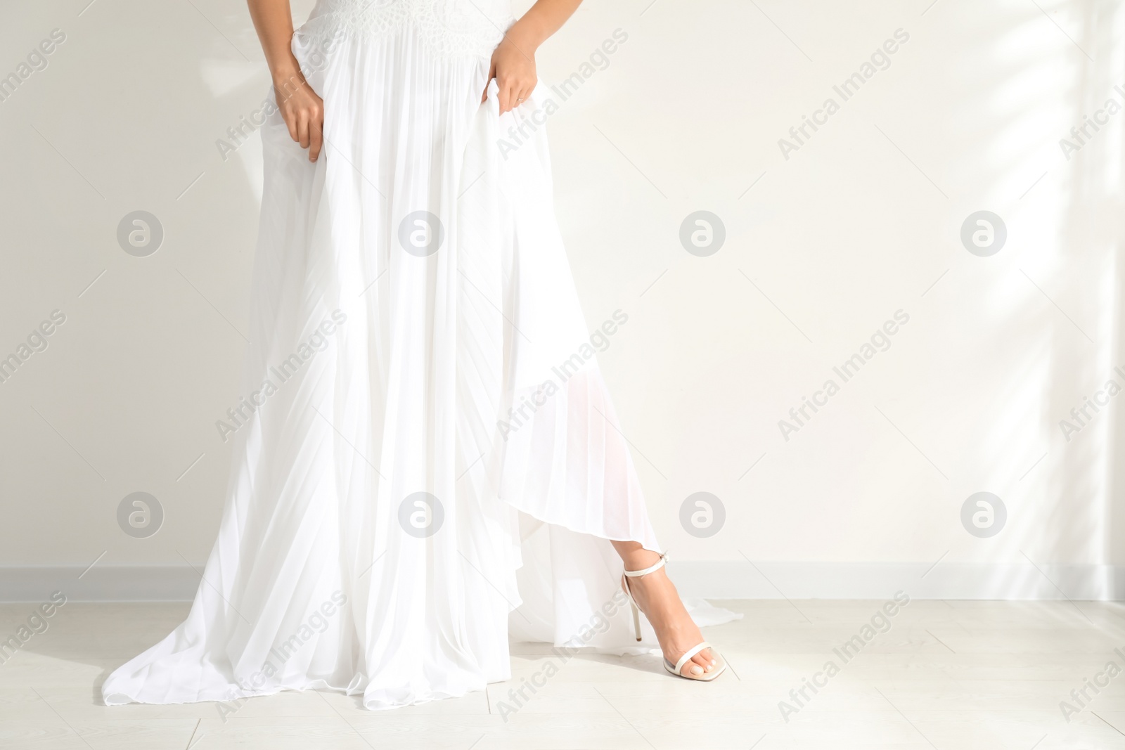 Photo of Young bride wearing beautiful wedding dress near light wall, closeup