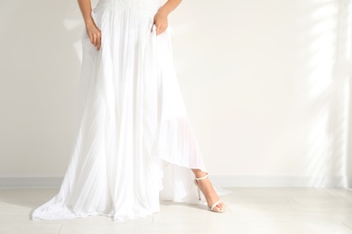 Young bride wearing beautiful wedding dress near light wall, closeup