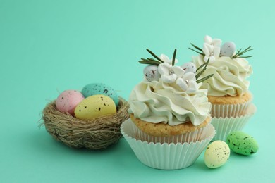 Photo of Tasty Easter cupcakes with vanilla cream and festive decor on turquoise background