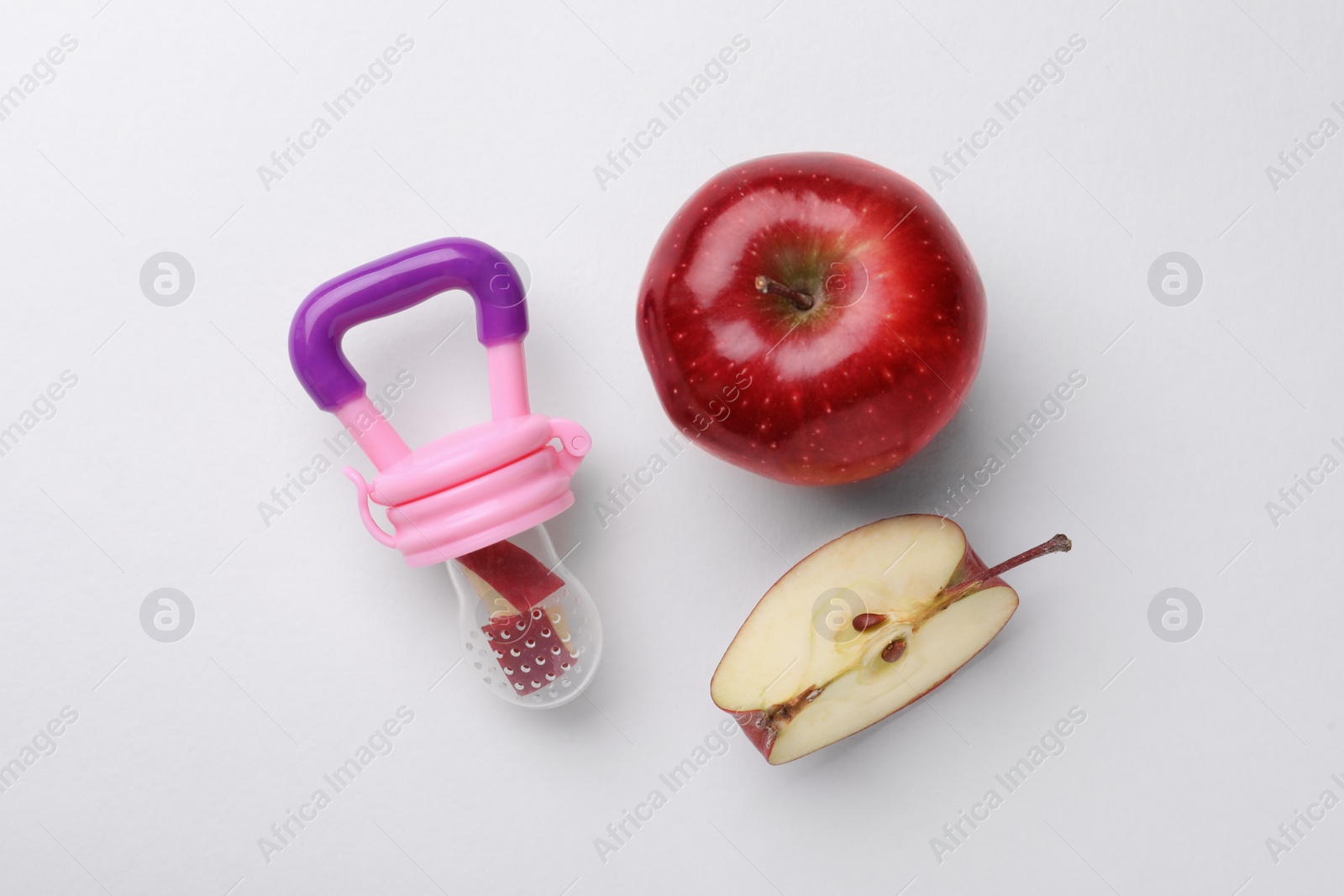 Photo of Nibbler with fresh apple on white background, flat lay. Baby feeder