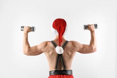 Young muscular man in Santa hat with dumbbells on white background