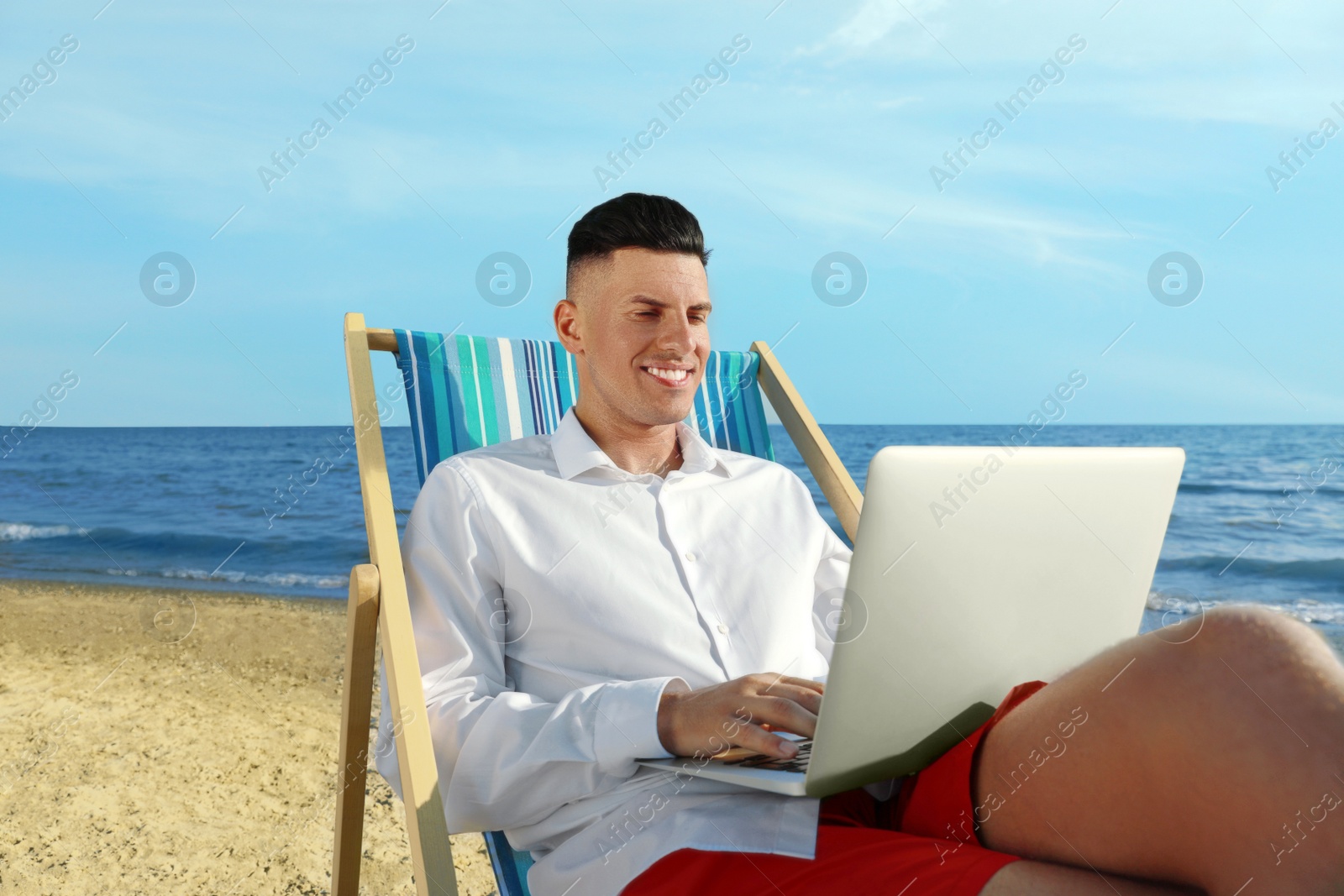 Photo of Happy man working with laptop on beach. Business trip