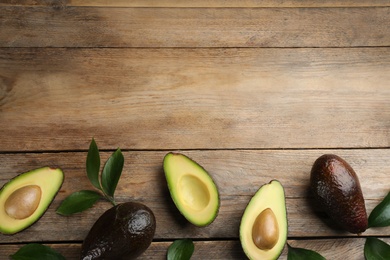 Photo of Whole and cut avocados with green leaves on wooden table, flat lay. Space for text