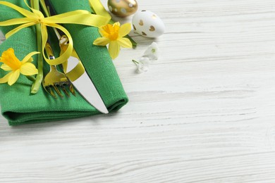 Photo of Cutlery set, Easter eggs and narcissuses on white wooden table, space for text