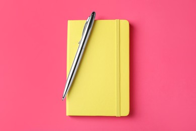 Photo of New stylish planner with hard cover and pen on pink background, top view