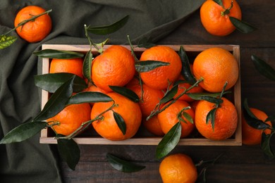 Photo of Fresh ripe tangerines with green leaves in crate on wooden table, flat lay