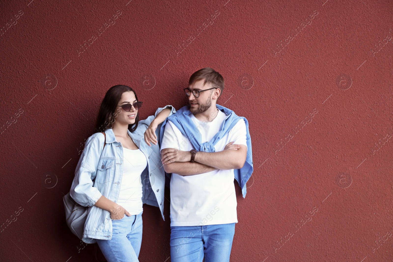 Photo of Young hipster couple in stylish jeans posing near color wall
