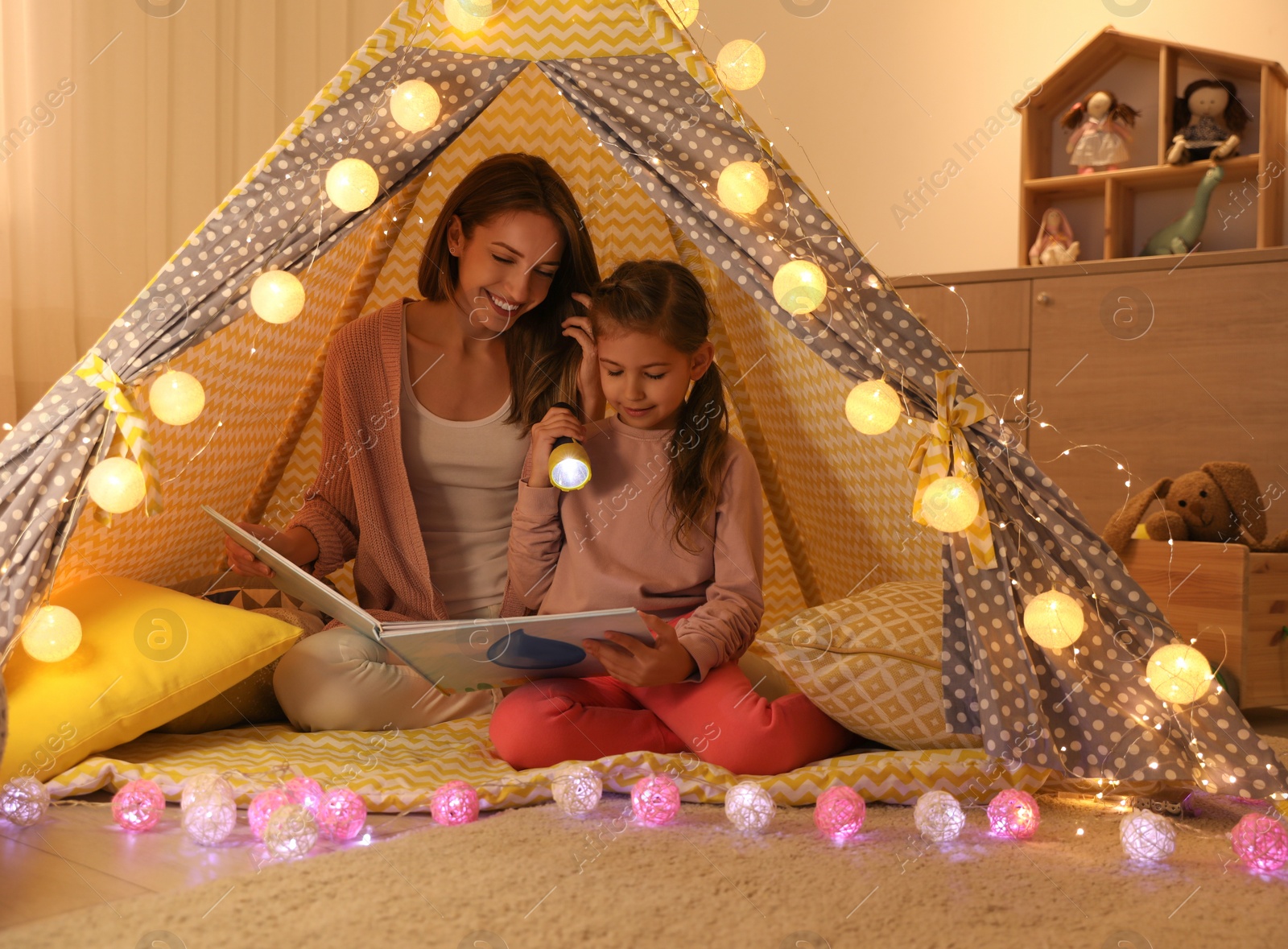 Photo of Mother and daughter with flashlight reading book in play tent
