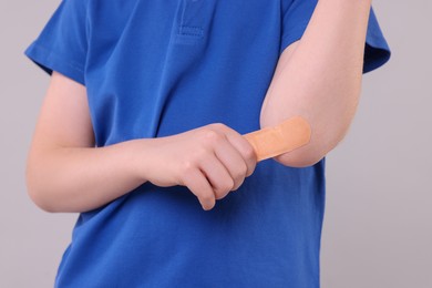 Photo of Little boy putting sticking plaster onto elbow against light grey background, closeup