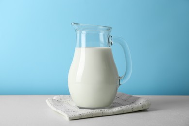 Photo of One jug of fresh milk on white table against light blue background