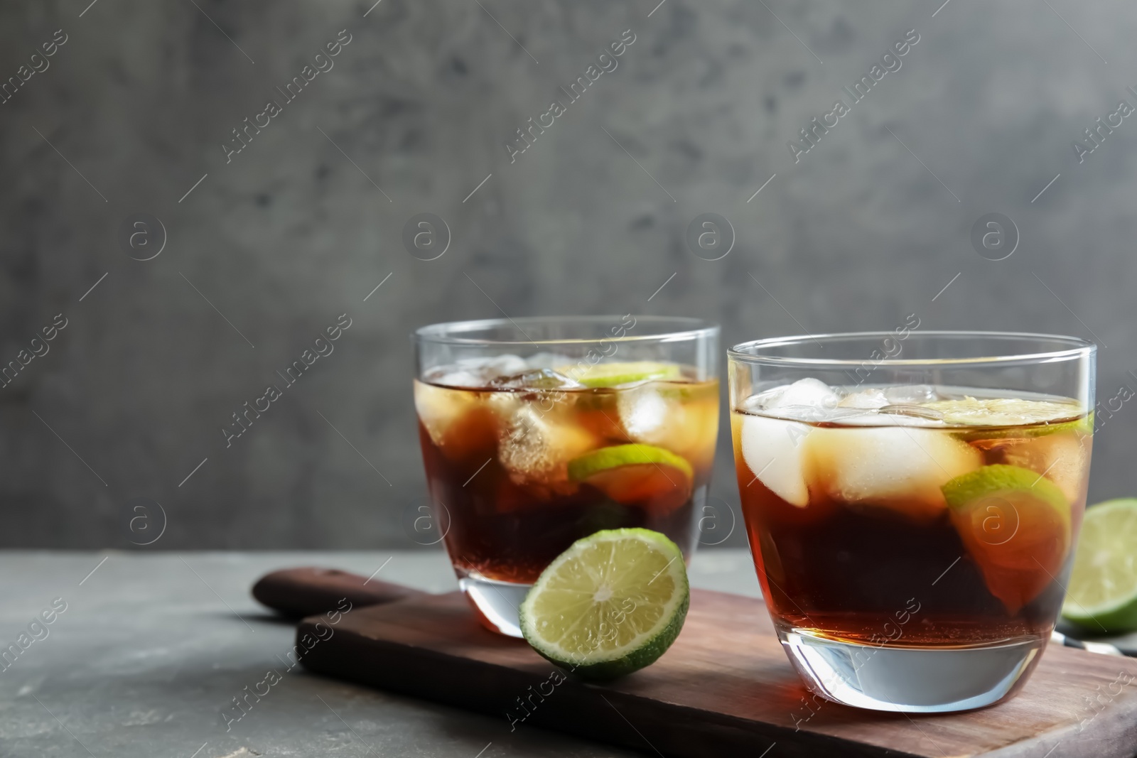 Photo of Glasses of cocktail with cola, ice and cut lime on table. Space for text