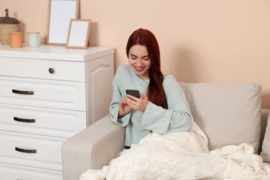 Happy woman with red dyed hair using smartphone at home