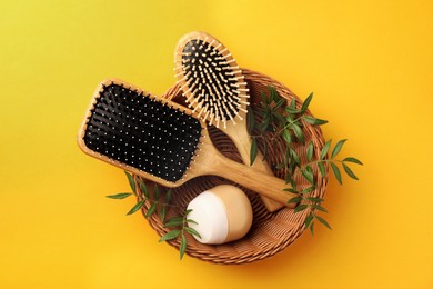 Photo of Wooden hairbrushes, jar of cosmetic product and leaves on orange background, top view