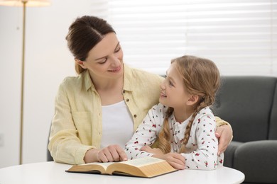Girl and her godparent reading Bible together at table indoors