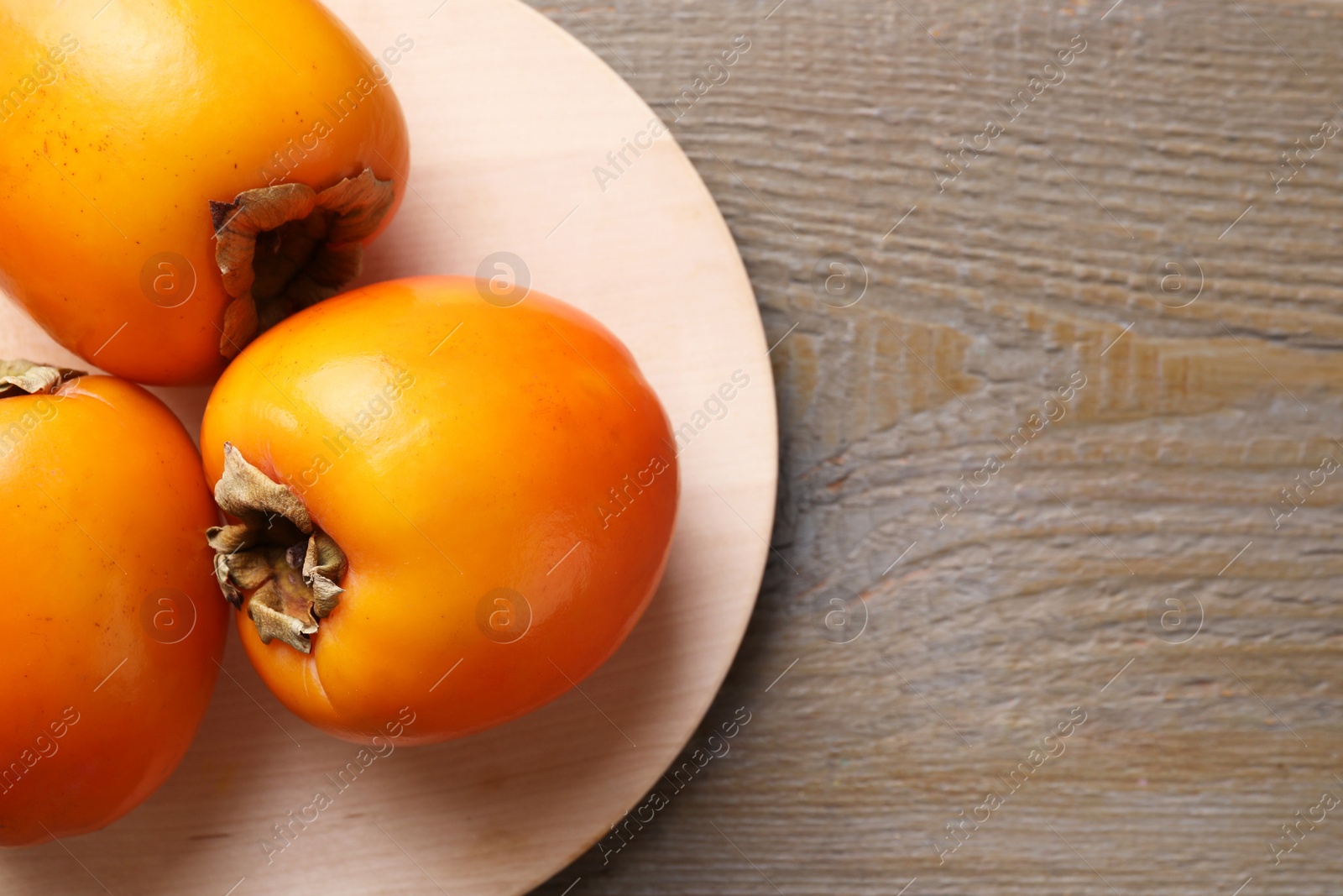 Photo of Delicious ripe persimmons on wooden table, top view. Space for text