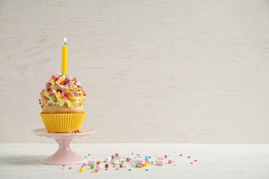 Birthday cupcake with candle on white table against wooden background. Space for text