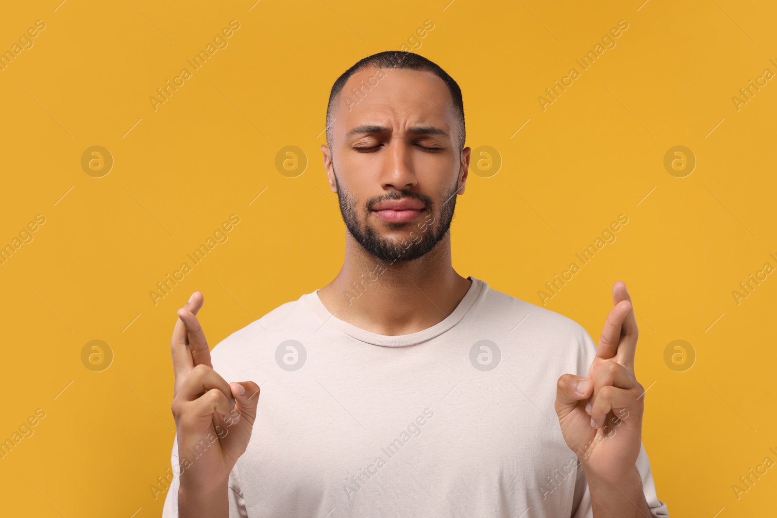 Photo of Young man crossing his fingers on orange background