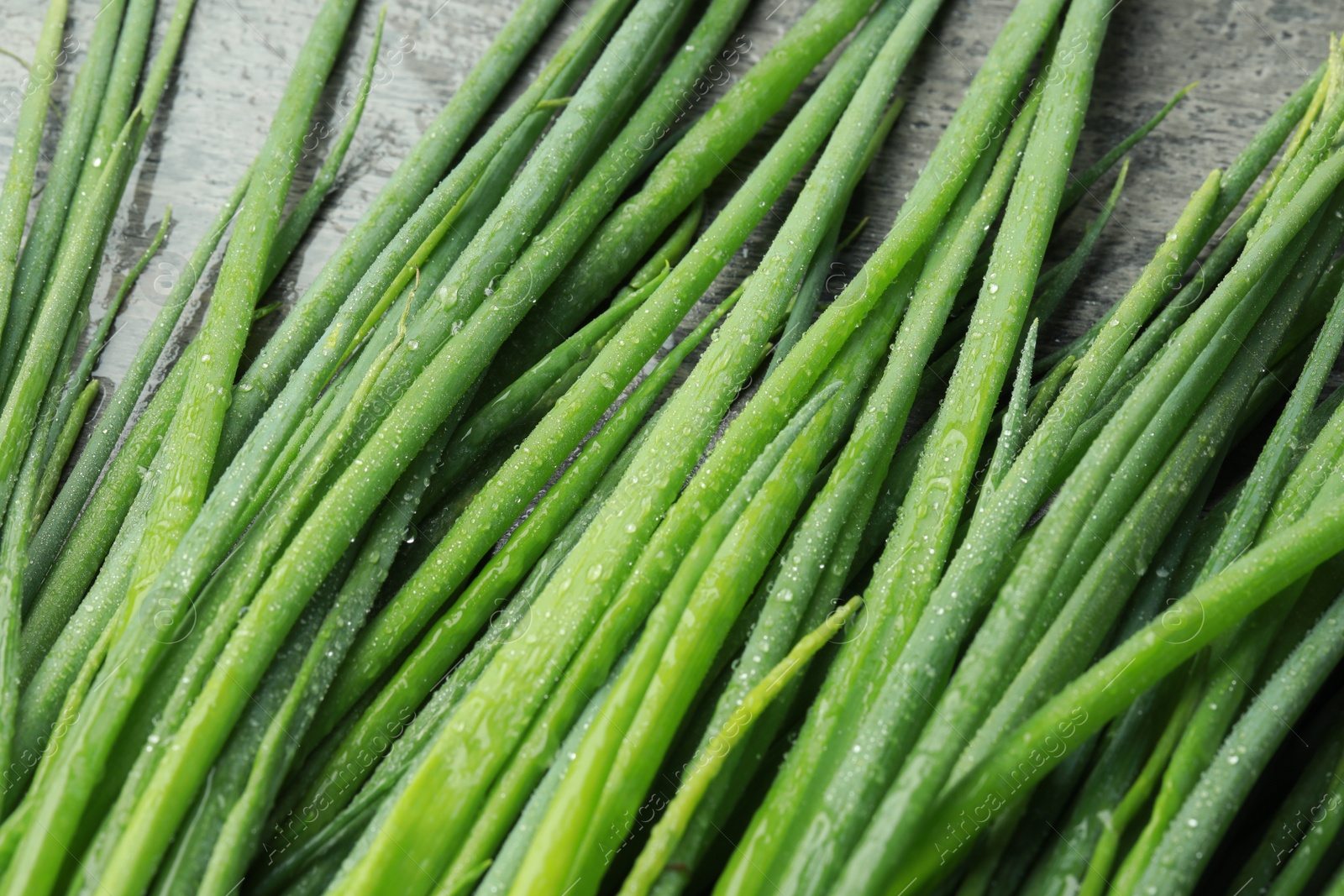 Photo of Fresh green spring onions with water drops on grey table, closeup